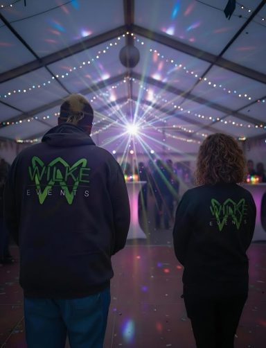 Zwei Personen mit Kapuzenpullovern stehen vor einer festlichen Beleuchtung in einem Zelt.